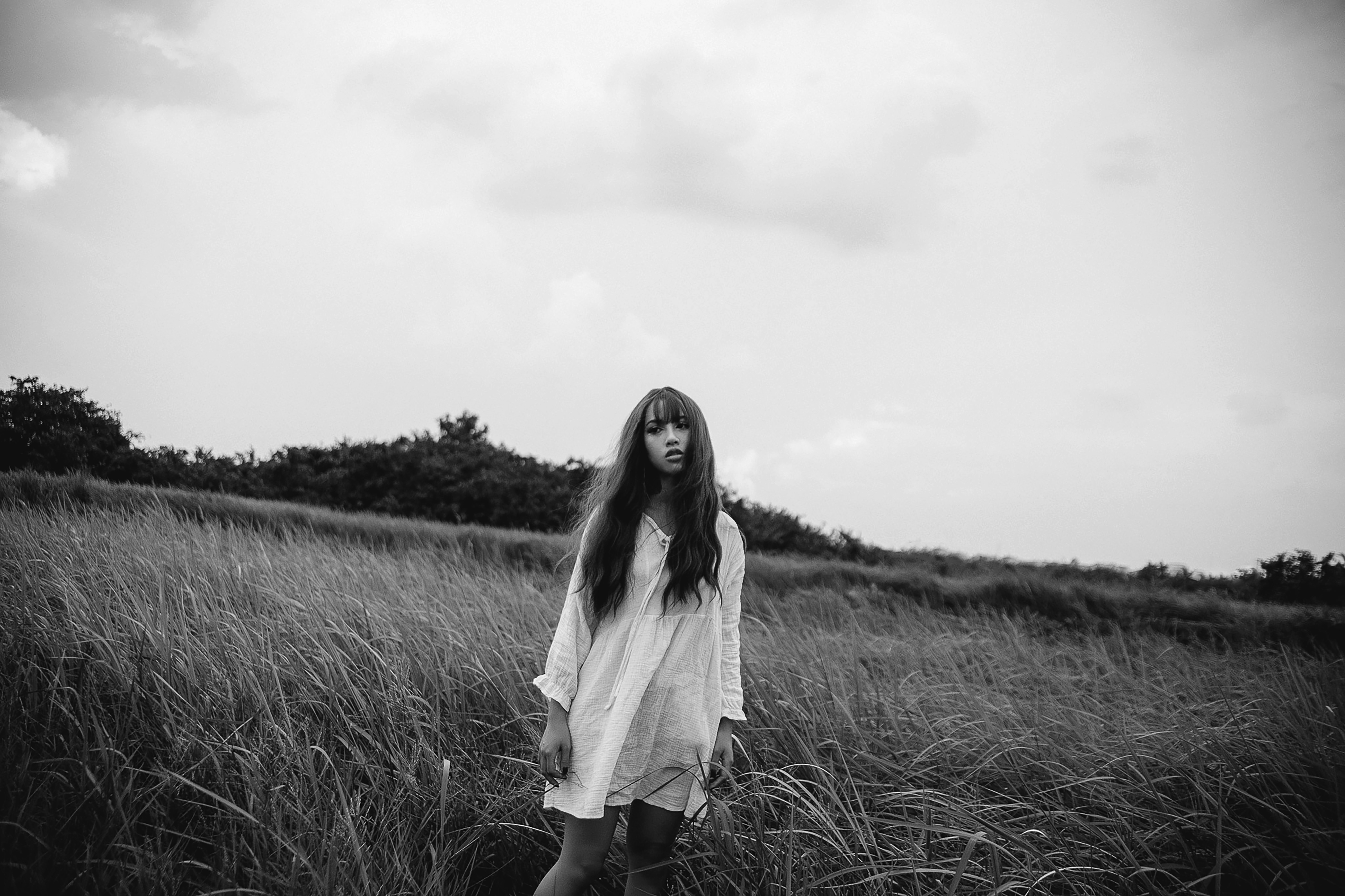 grayscale photo of woman in white dress standing on grass field