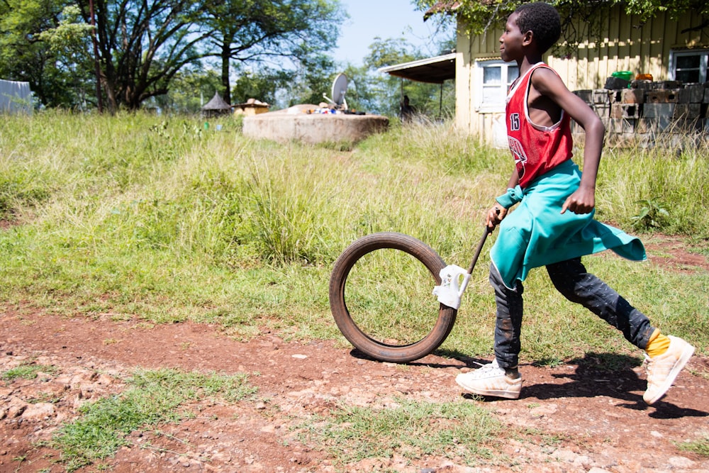 boy in red t-shirt and black pants holding brown wheel during daytime