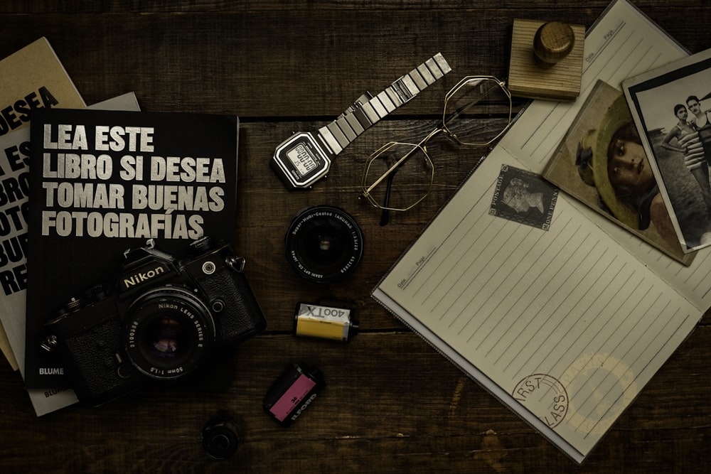 black and silver dslr camera beside white ruled paper on brown wooden table