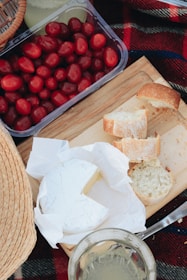A picnic setup at a campsite with fresh bread, cheese, and fruit on a checkered cloth.