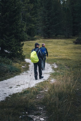 man in blue jacket and yellow backpack walking on dirt road