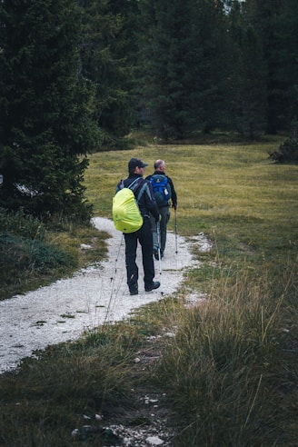 man in blue jacket and yellow backpack walking on dirt road