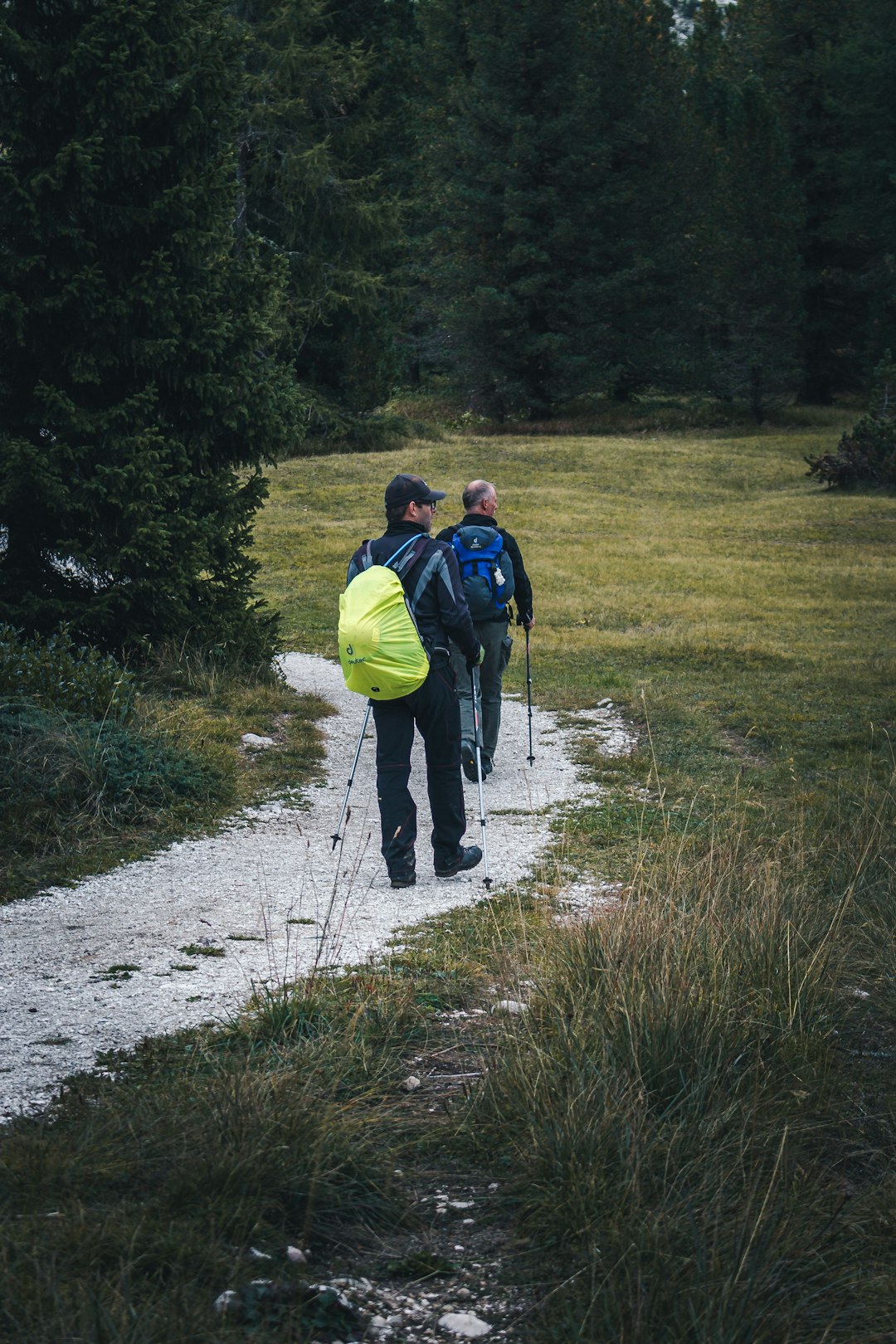 man in blue jacket and yellow backpack walking on dirt road