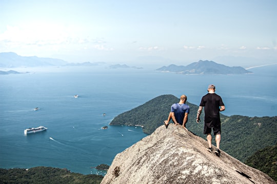 man in black shirt standing on rock formation near body of water during daytime in Ilha Grande Brasil