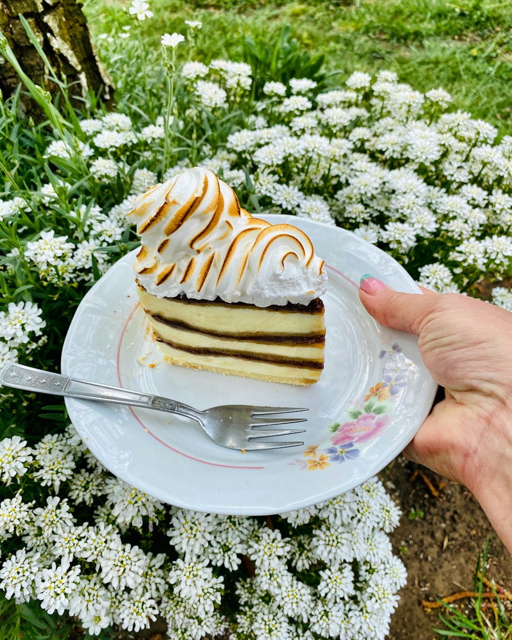 person holding a stainless steel fork with a brown pastry on a white ceramic plate