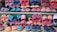A variety of colorful, handcrafted shoes arranged in neat rows. The shoes display intricate patterns and vibrant colors such as red, blue, orange, and black. Some feature detailed embroidery or unique designs, highlighting artisanal craftsmanship.