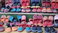 A variety of colorful, handcrafted shoes arranged in neat rows. The shoes display intricate patterns and vibrant colors such as red, blue, orange, and black. Some feature detailed embroidery or unique designs, highlighting artisanal craftsmanship.
