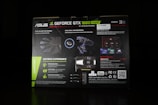 The image features the packaging of an ASUS GeForce GTX 1660 Super graphics card. The box highlights various features such as 'Wing-Blade Fan Design', 'Dual Ball Fan Bearings', and 'Geforce Experience'. It includes visuals of the fan blades and bearing components alongside descriptions of product specifications and software suite capabilities. The packaging is predominantly black with green accents and white text.