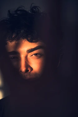 A striking portrait of Danny Goldenballs bathed in dark gold light, with a mischievous grin and dramatic shadows.