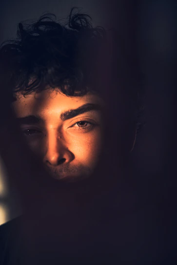 A striking portrait of Danny Goldenballs bathed in dark gold light, with a mischievous grin and dramatic shadows.