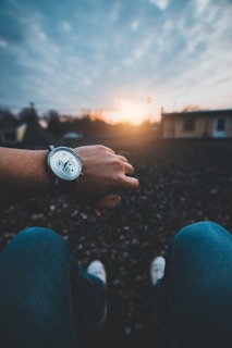 A watch face reflecting the sunset while worn on a wrist outdoors.