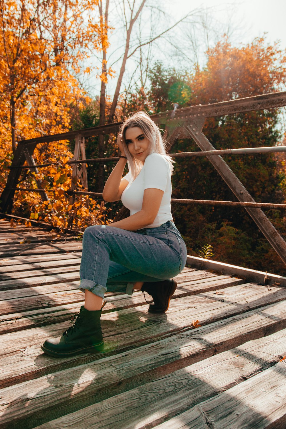 woman in white tank top and blue denim jeans sitting on brown wooden stairs