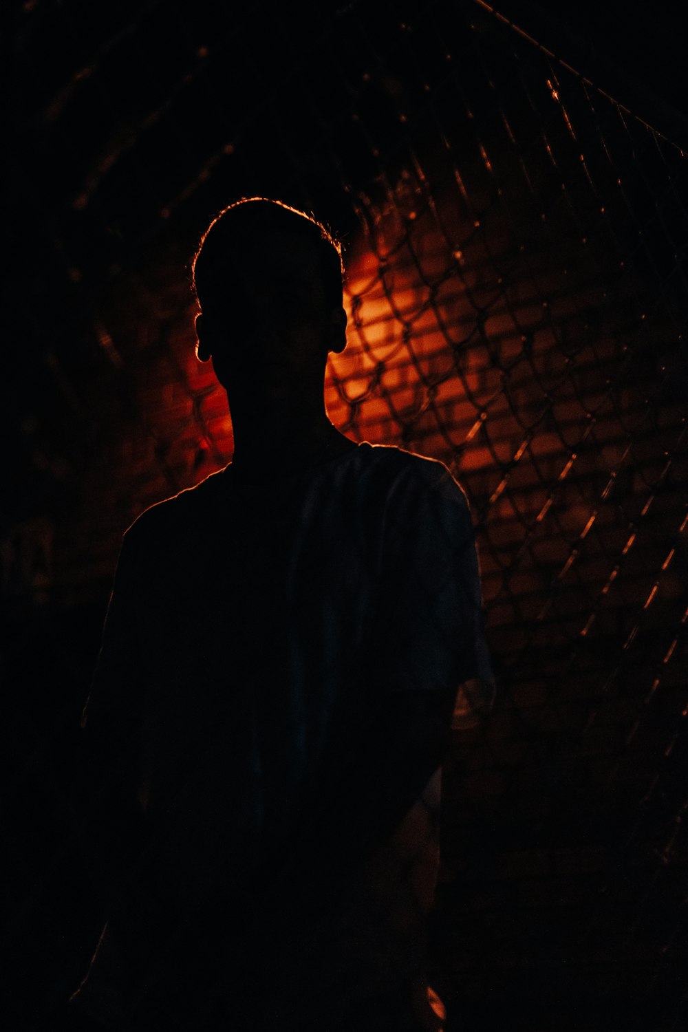 man in white crew neck shirt standing near brown brick wall