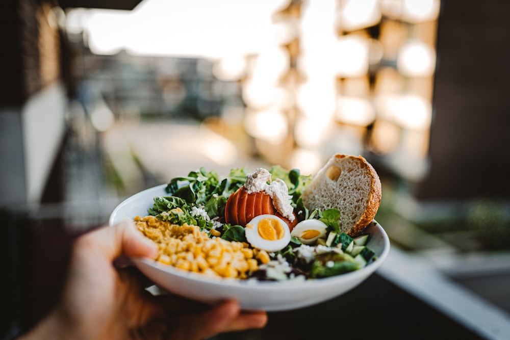 person holding white ceramic plate with sliced bread and vegetables