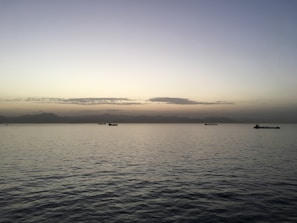 A panoramic view of a dark-hulled crude oil tanker gliding through calm, twilight seas under a navy sky.