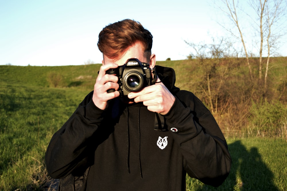 man in black hoodie holding black nikon dslr camera