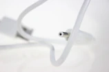 A close-up view of a white cable with a cylindrical connector in focus, set against a blurred white background. The cable curves gracefully, leading the eye to the connector tip.