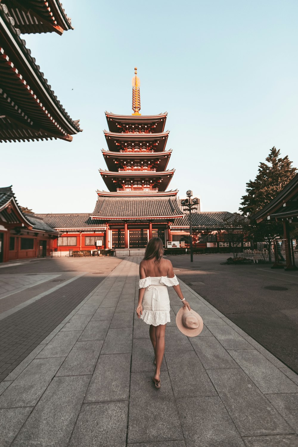 woman in white dress holding white umbrella walking on gray concrete pathway during daytime