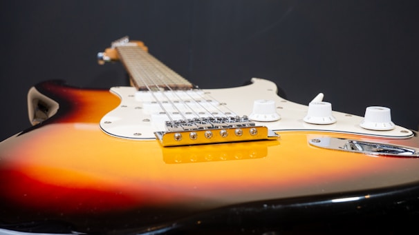 A close-up of an electric guitar featuring a sunburst finish, white pickguard, and several control knobs located on the body. The focus is on the bridge and the strings, highlighting the instrument's craftsmanship and design.