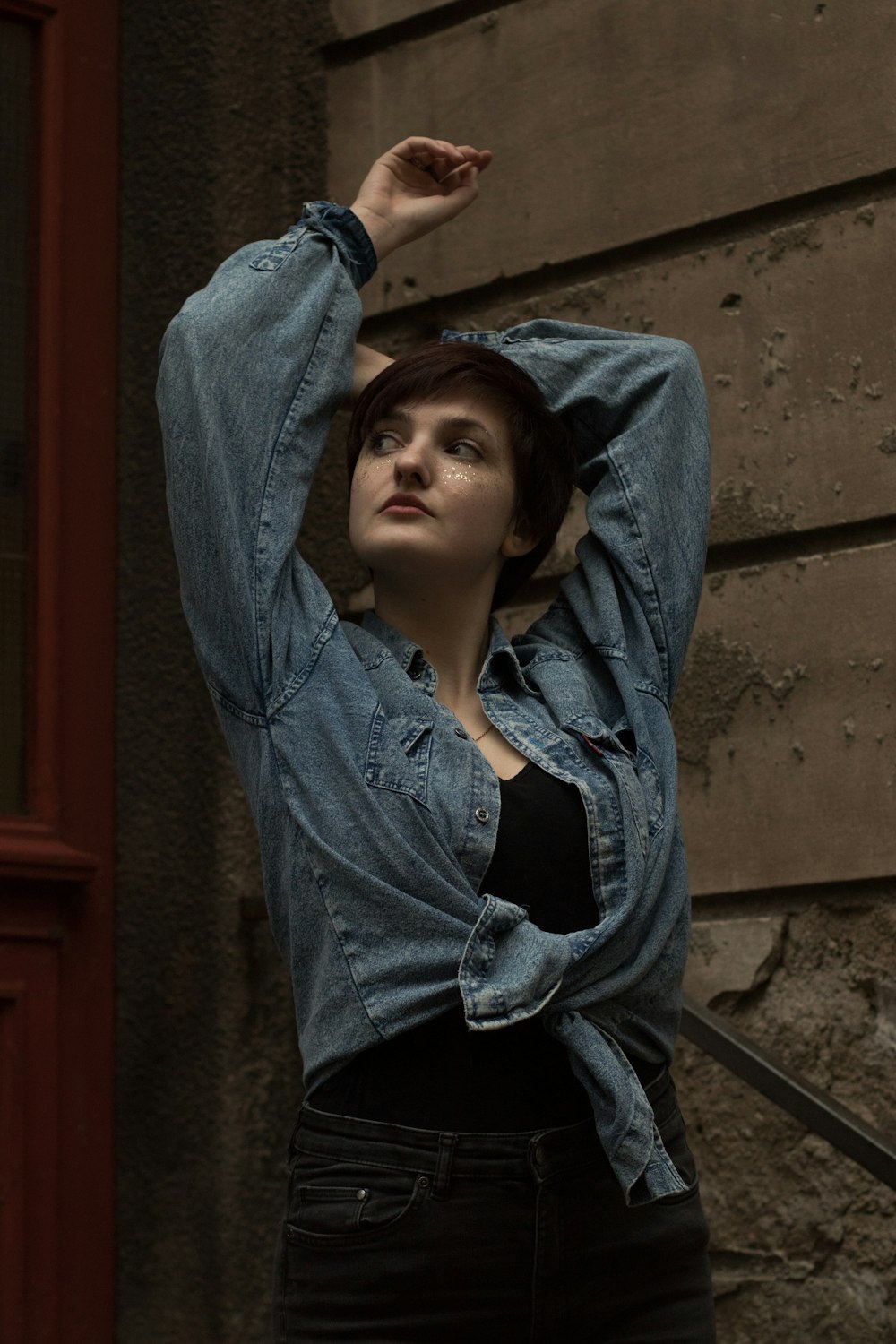 woman in blue denim jacket leaning on brown concrete wall during daytime