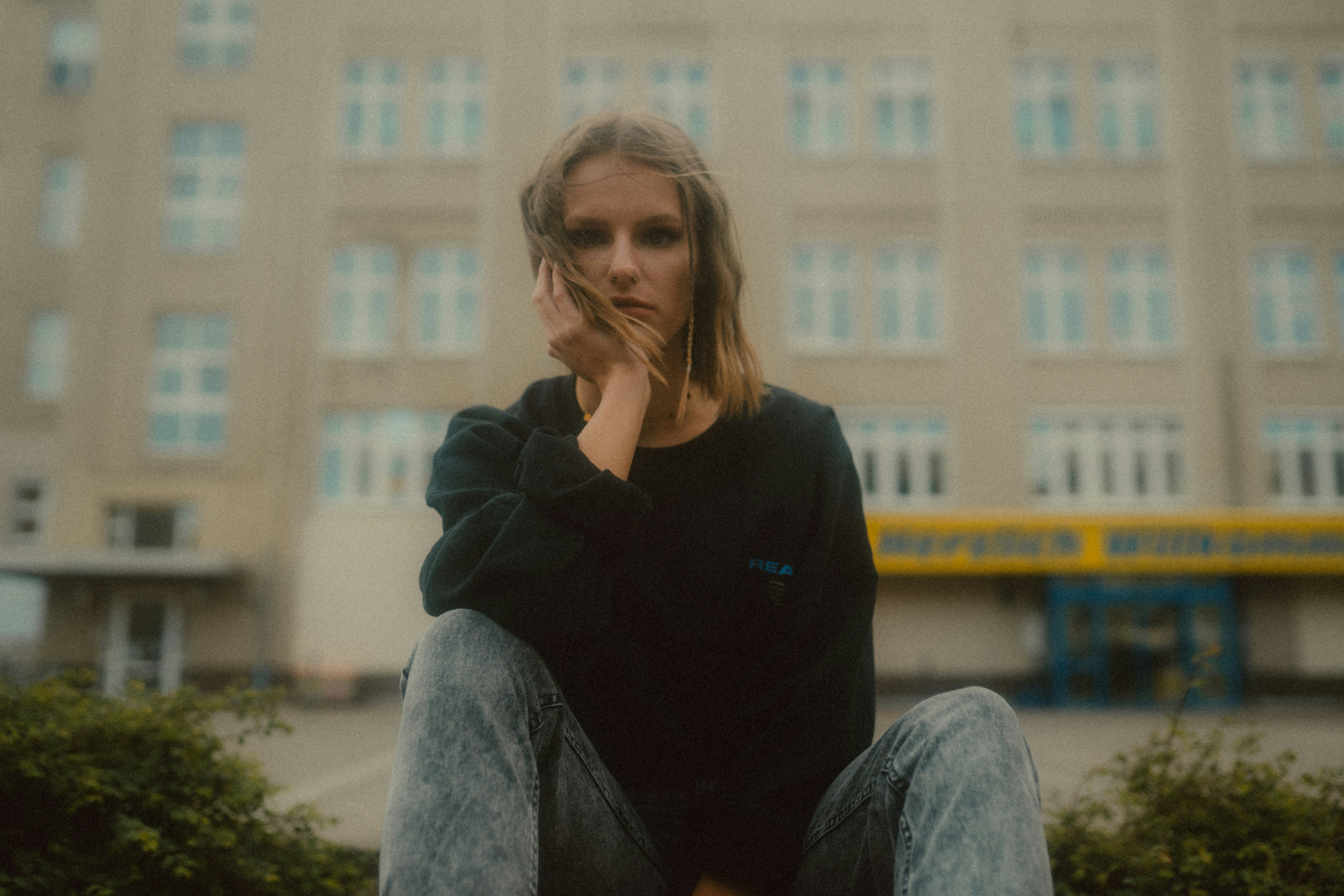 woman in black long sleeve shirt and gray denim jeans sitting on brown wooden chair