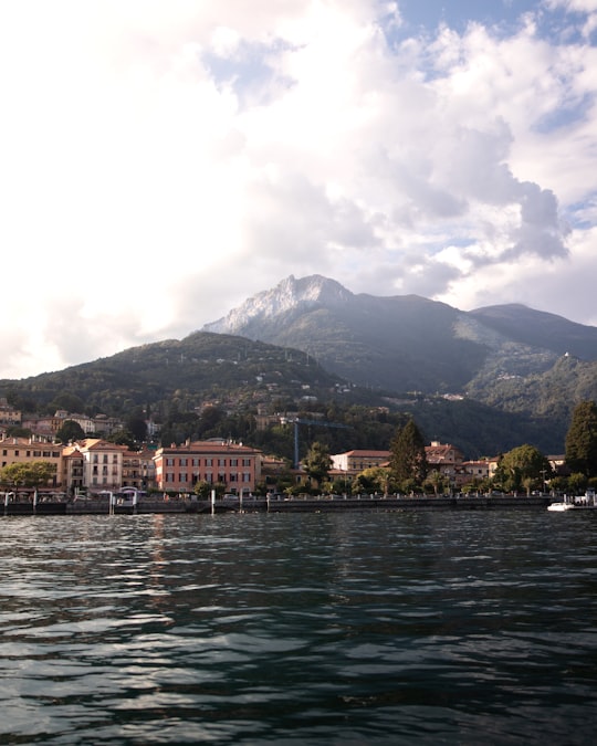 white and brown concrete building near body of water and mountain under white clouds during daytime in Lake Como Italy