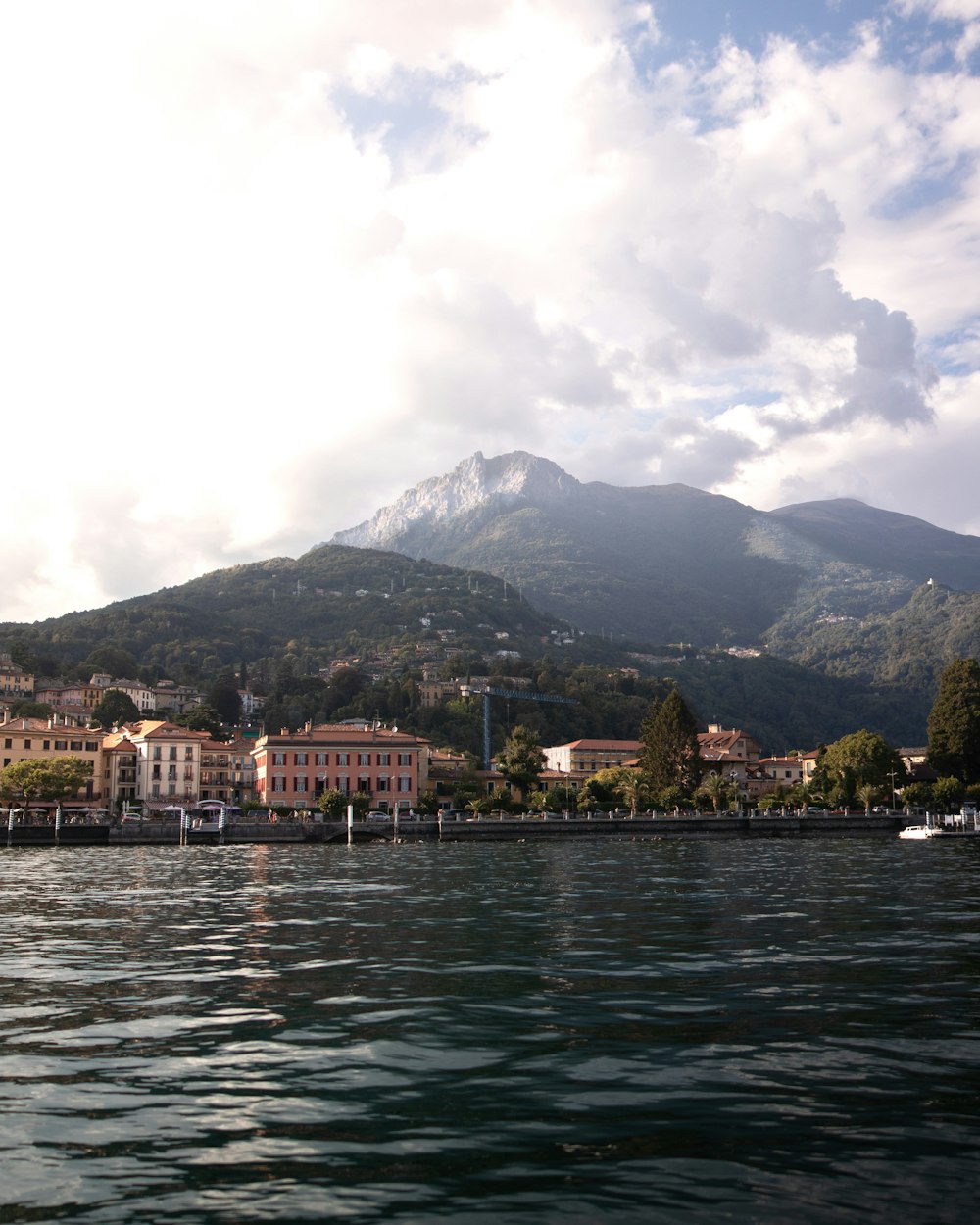 white and brown concrete building near body of water and mountain under white clouds during daytime