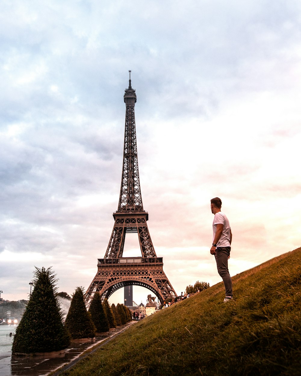 man in white shirt and black pants standing on green grass near eiffel tower during daytime
