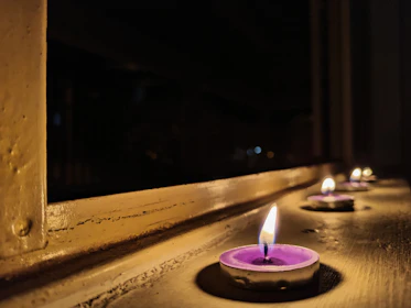 A glowing amethyst crystal surrounded by flickering candles in a dark room.