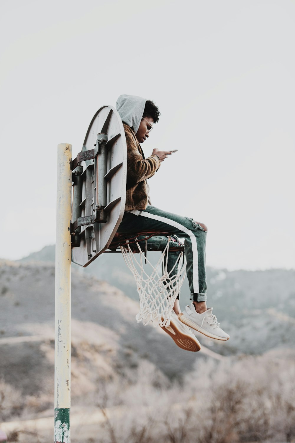 woman in brown jacket sitting on basketball hoop during daytime