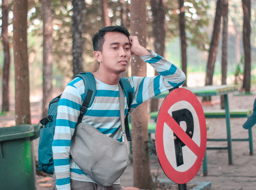 man in blue red and white striped polo shirt standing near brown wooden post during daytime