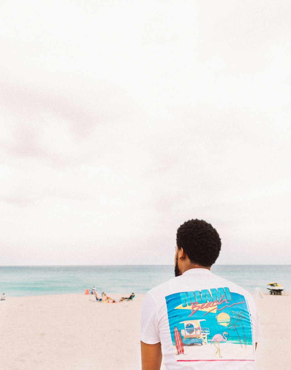 흰색과 파란색의 크루넥 티셔츠를 입은 남자가 낮에 해변에 서 있습니다.