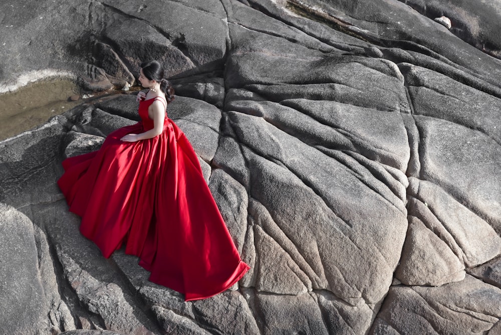 woman in red dress sitting on gray rock