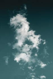 A vertical cloud formation set against a deep greenish-blue sky. The wispy clouds have an irregular shape, with some denser, whiter portions and others more diffused and airy.