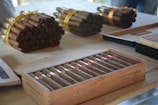 A wooden table displays bundles of cigars tied with yellow ribbons and a wooden box labeled 'Partagas Habana Cuba' containing neatly arranged cigars. The mood is calm and sophisticated.
