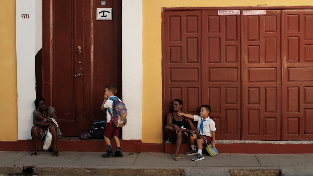 3 children sitting on floor near red wooden door