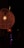 A warmly lit, intricately woven lamp hangs in the dark, radiating a soft orange glow. The texture of the lamp's material adds a rustic charm to the overall aesthetic. In the background, other smaller lights are visible, faintly illuminating the surrounding area.