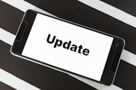 A smartphone displaying the word 'Update' on its screen is placed on a black and white striped surface. The phone is in landscape orientation, and the image focuses on the screen’s content.