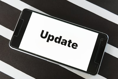 A smartphone displaying the word 'Update' on its screen is placed on a black and white striped surface. The phone is in landscape orientation, and the image focuses on the screen’s content.