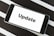 A smartphone displaying the word 'Update' on its screen is placed on a black and white striped surface. The phone is in landscape orientation, and the image focuses on the screen’s content.