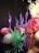 A vibrant and intricate glass sculpture composed of swirling purple, red, and yellow forms, along with spherical glass elements. The pieces are artistically arranged, creating a visually dynamic display with reflections on a glossy black surface.