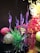 A vibrant and intricate glass sculpture composed of swirling purple, red, and yellow forms, along with spherical glass elements. The pieces are artistically arranged, creating a visually dynamic display with reflections on a glossy black surface.
