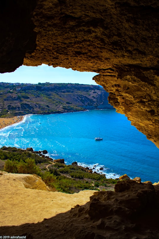 brown rock formation near body of water during daytime in Tal-Mixta Cave Malta