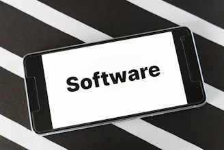A smartphone is placed on a surface with a black and white striped pattern. The phone screen displays the word 'Software' in bold black text against a white background.