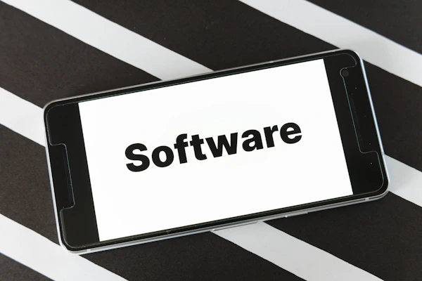 A smartphone is placed on a surface with a black and white striped pattern. The phone screen displays the word 'Software' in bold black text against a white background.