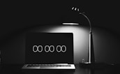 A minimalist setup with a laptop displaying a digital clock set at '00:00', beside a modern desk lamp casting a soft glow over the scene, creating contrast in an otherwise dark environment.