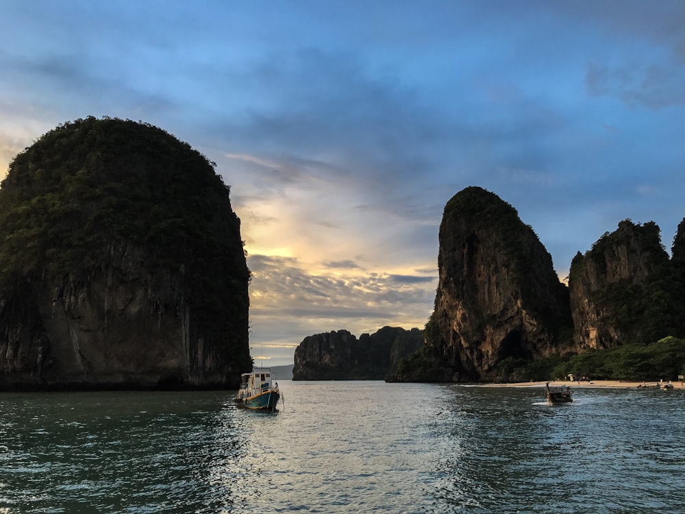 white and blue boat on sea near brown rock formation during daytime