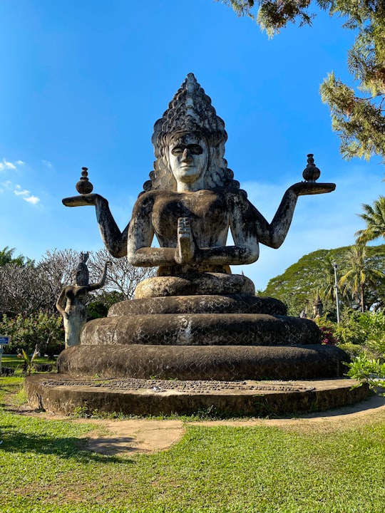 black concrete statue on green grass field during daytime in Buddha Park Laos