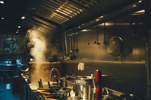Cocina industrial en operación, donde el vapor cargado de grasa sube a la campana