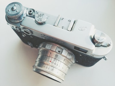 An overhead view of a vintage camera with manual dials and a silver lens prominently displayed. The camera features textured black material on its body and intricate markings on the lens indicating focus distances. The knobs and dials are crafted with precision, adding to the classic aesthetic of the camera.